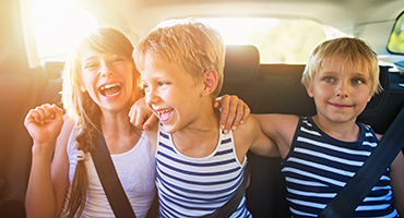 Three children sitting in the back seat of a car laughing