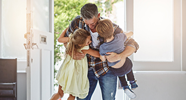 Dad hugging two kids as he enters front door