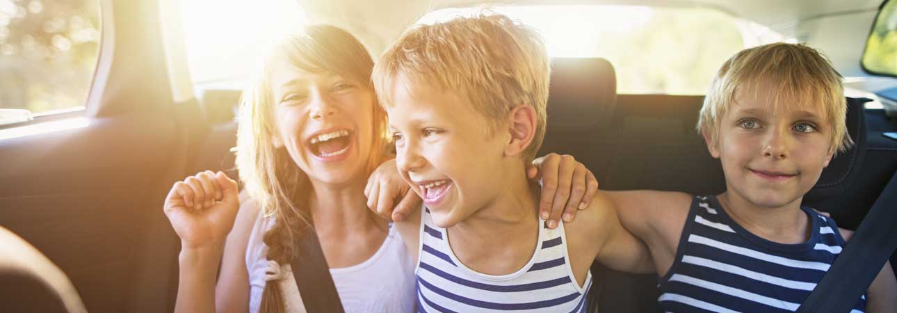 Three children sitting in the back seat of a car laughing