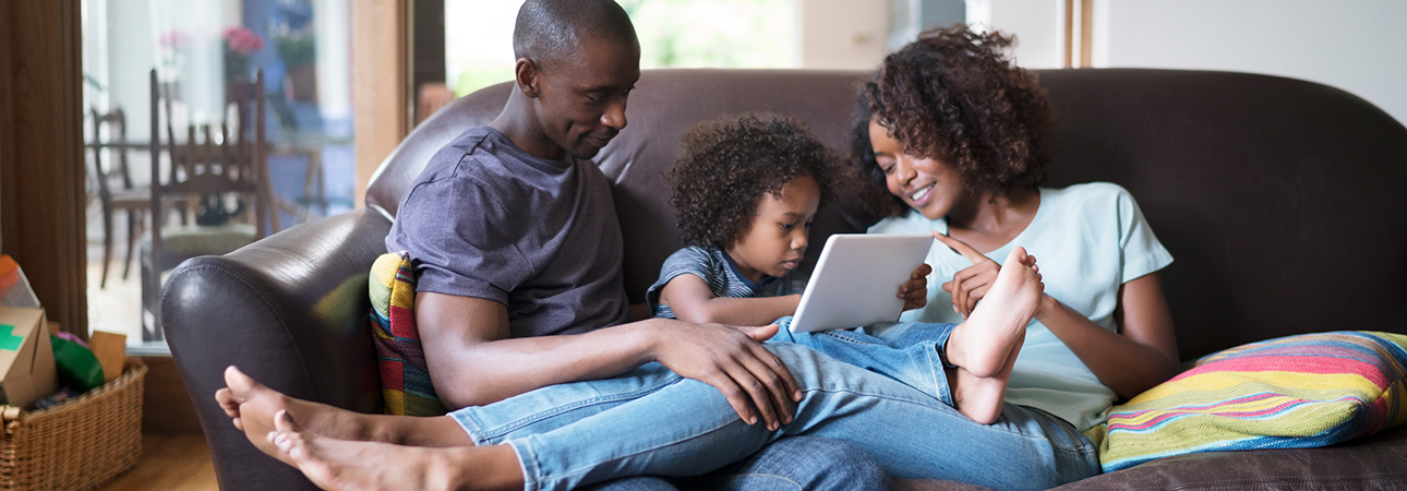 Mom, dad, and daughter sitting on couch looking at computer