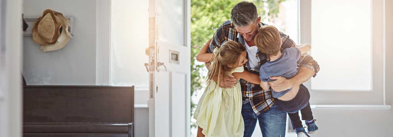 A son and daughter hugging their Dad as he walks in the front door